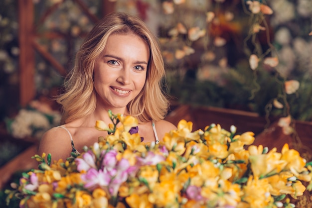 Foto gratuita primo piano del mazzo dei fiori gialli davanti alla giovane donna bionda che guarda alla macchina fotografica