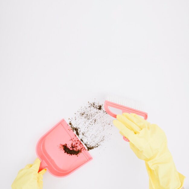 Close-up of yellow gloved hands sweeping dust into dustpan on white background