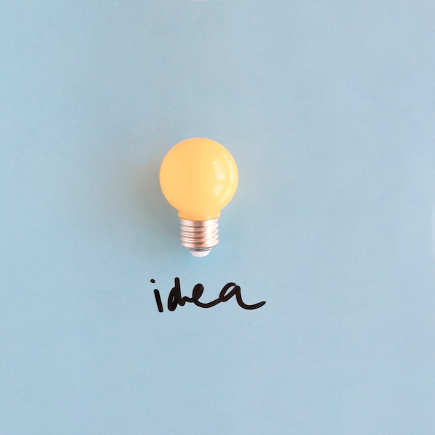 Close-up of yellow light bulb with idea word on blue background