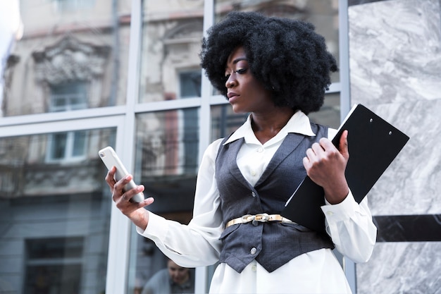 Close-up of a young african businesswoman holding clipboard using mobile phone