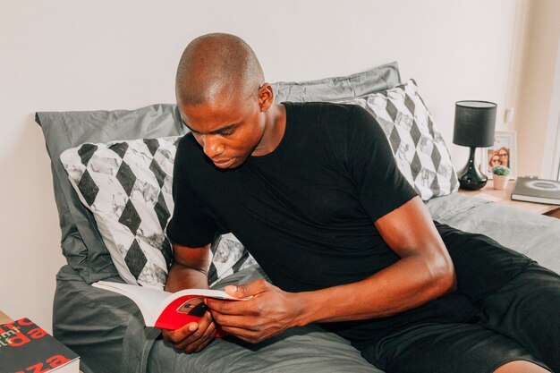 Close-up of a young african man lying on bed reading book