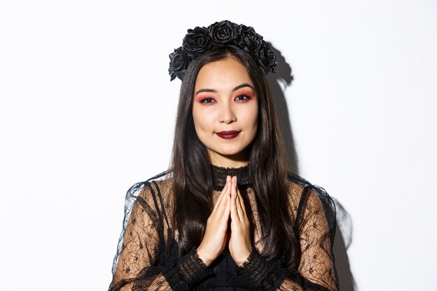 黒のゴシックドレスと祈りで手をつないで花輪、魔女の衣装を着てハロウィーンを祝っている女の子の若いアジアの女性のクローズアップ。
