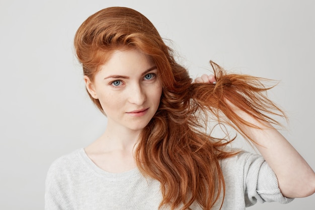 Close up of young beautiful ginger girl smiling touching hair .