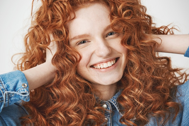 Close up of young beautiful ginger girl touching hair smiling