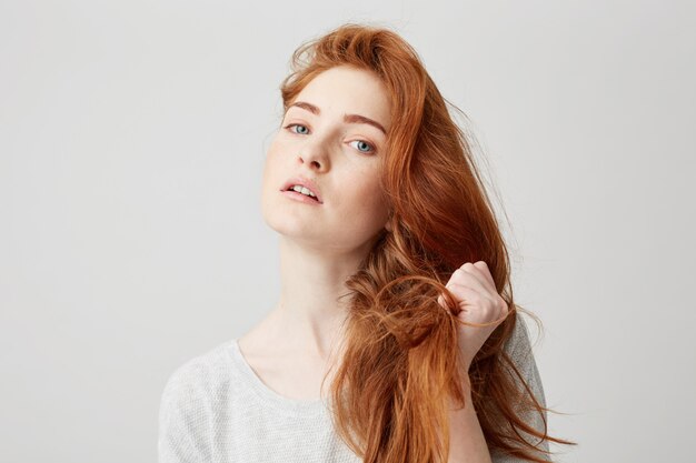 Close up of young beautiful ginger girl touching hair .