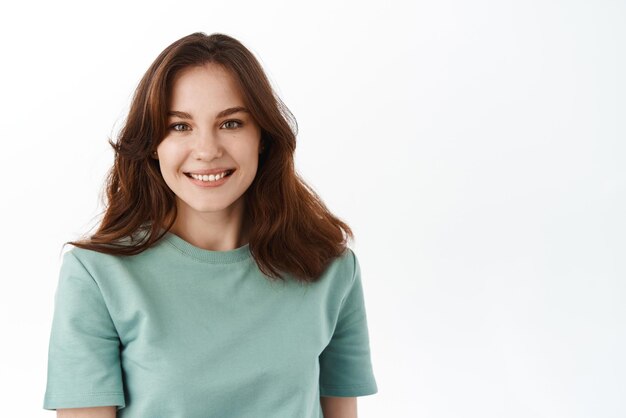 Close up of young beautiful woman with fresh clean skin natural nude make up smiling broadly at camera and looking happy standing against white background