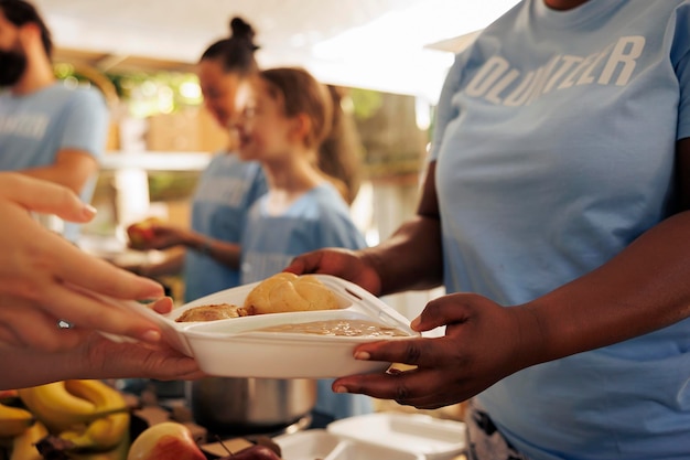 Free photo close-up of a young black woman hands distributing fresh produce to needy homeless people at a food drive. detailed image of free food being shared to a poor less privileged caucasian person.