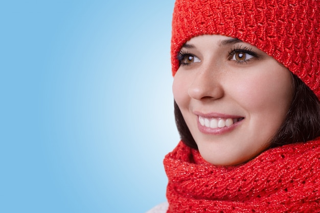 スカーフ付きの暖かい帽子をかぶって素敵な心地よい笑顔の若い茶色の目をした女性のクローズアップ