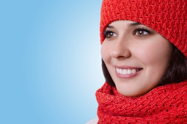 A close-up of a young brown-eyed woman with nice pleasant smile wearing warm hat with scarf