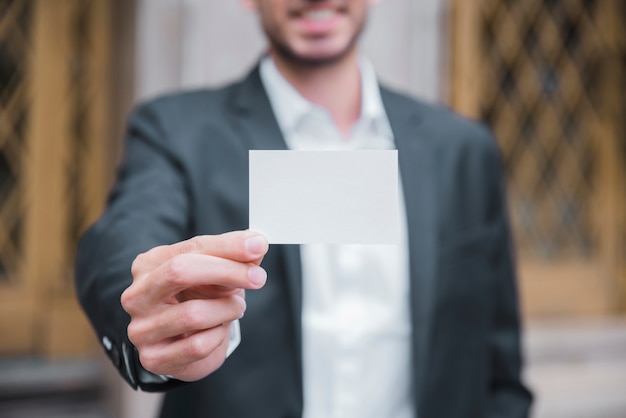 Close-up of a young businessman showing white visiting card in front of camera