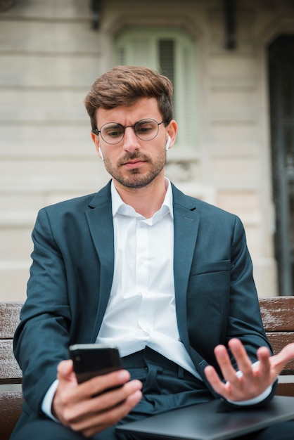 Close-up of young businessman talking on mobile phone with wireless earphone in his ears