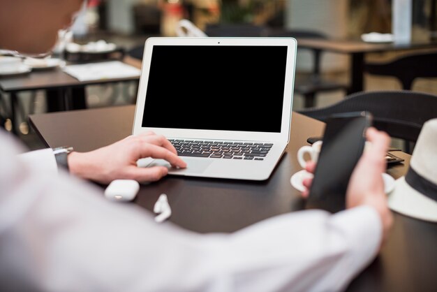 Close-up of a young businessman using mobile phone and laptop at workplace