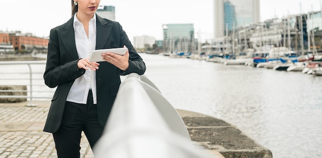 Free photo close-up of a young businesswoman leaning on railing near the harbor using mobile phone