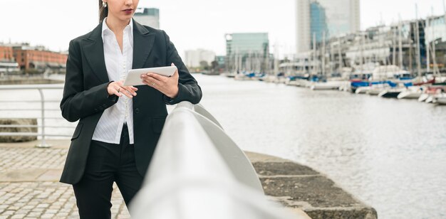 Close-up of a young businesswoman leaning on railing near the harbor using mobile phone
