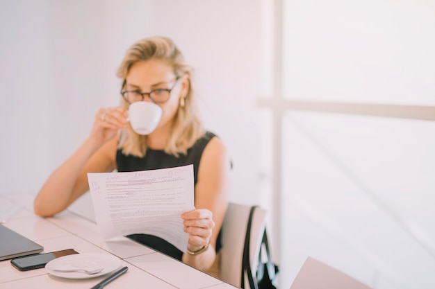 Foto gratuita primo piano di giovane donna di affari che legge il documento mentre bevendo il caffè