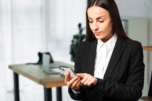 Close-up of a young businesswoman standing in the office touching smartphone