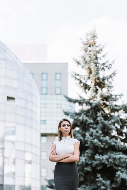 Close-up of a young businesswoman with arms crossed standing in front of modern building