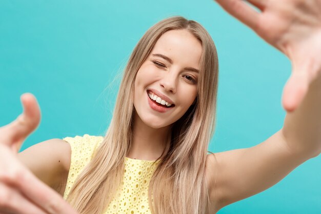 Close-up Young Caucasian woman face and eye care and she making frame with hands isolated over pastel blue background.