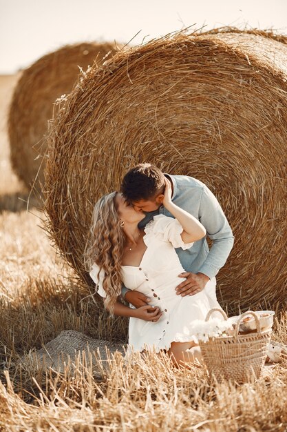 Close up of a young couple sitting at the wheat field. People sits on haystack on meadow and embraces.