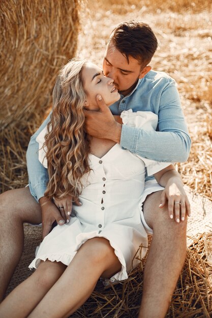 Close up of a young couple sitting at the wheat field. People sits on haystack on meadow and embraces.