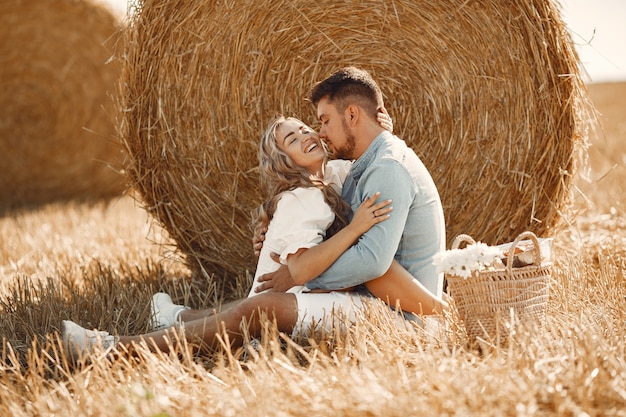 Close up of a young couple sitting at the wheat field. People sits on haystack on meadow and embraces.