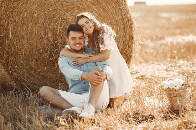 Close up of a young couple sitting at the wheat field. People sits on haystack on meadow and embraces.