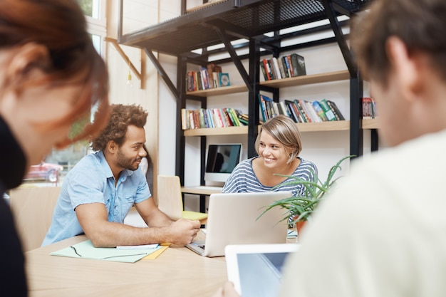 Free photo close up of young designers team sitting in coworking space at table, talking about profits of old projects, looking through statistics on laptop, having conversation