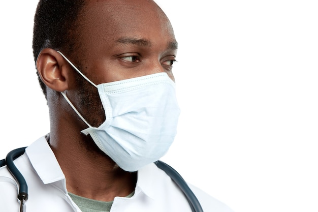 聴診器と白い壁に分離されたフェイス マスクを持つ若い医師を閉じる