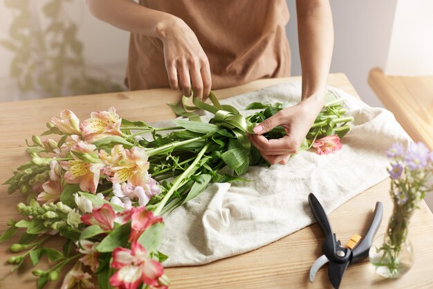 Close up of young female florist tying ribbon on bouquet at workplace.