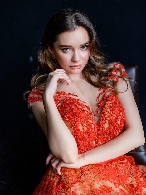 Close up of young girl in a red dress sits on a chair and looks at the camera