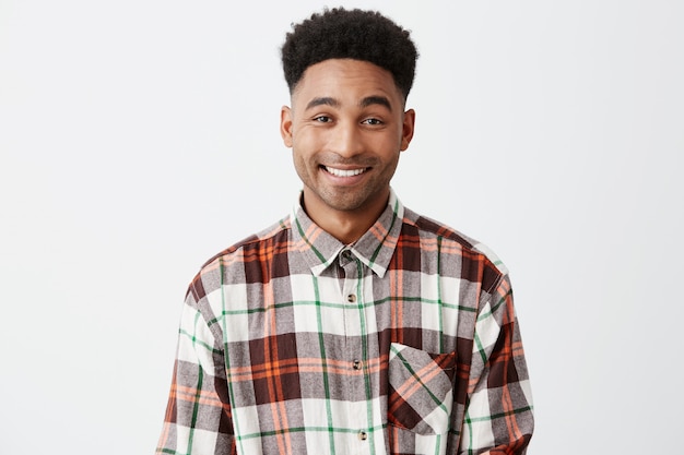 Close up of young good-looking dark-skinned cheerful american male with curly black hair in checkered shirt smiling with teeth with happy and relaxed face expression.