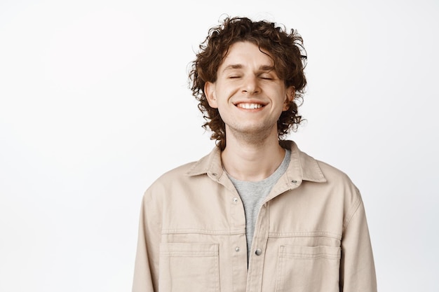 Close up of young guy close eyes and smile dreaming of something beautiful feeling happy breathing with satisfied face expression white background