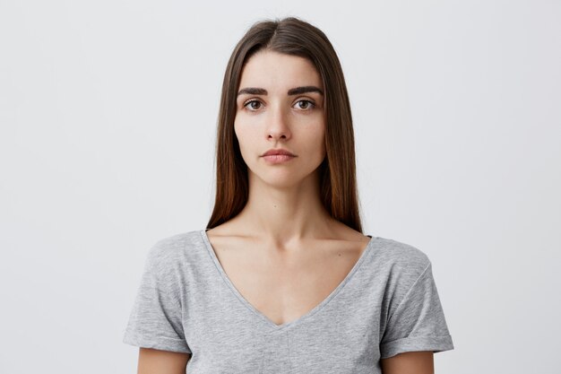 Close up of young handsome charming caucasian girl with long brown hair in gray t-shirt  with serious face expression. Woman getting photo for passport.