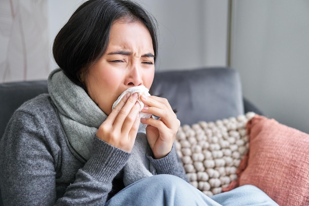 Free photo close up of young korean woman staying at home with cold sneezing in napking has runny nose concept