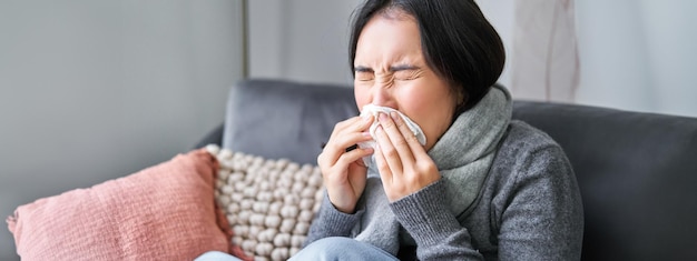 Free photo close up of young korean woman staying at home with cold sneezing in napking has runny nose concept