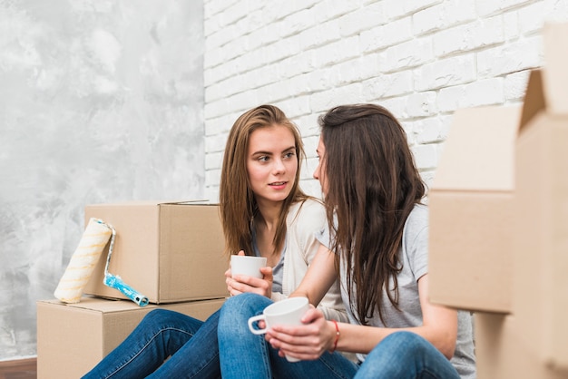 Free photo close-up of young lesbian couple holding cup of coffee sitting between the cardboard boxes