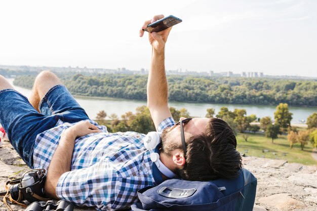 Close-up of a young male hiker lying on ground using mobile phone