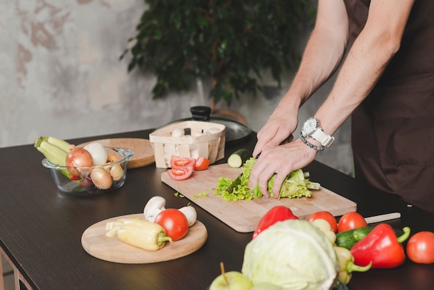 Free photo close-up of young man cutting lettuce with knife on chopping board