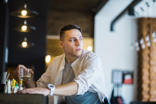 Free photo close-up of young man holding glass of whisky in the bar