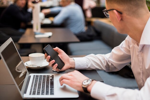 Close-up of a young man holding mobile in hand using digital tablet in caf�