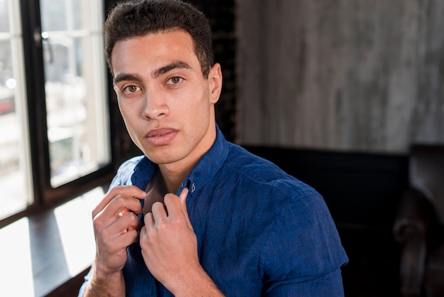 Close-up of a young man holding a shirt collar with his hand looking at camera