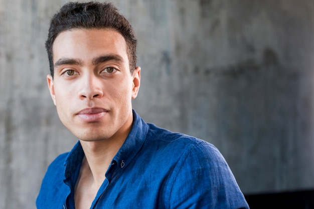 Close-up of a young man looking at camera against grey wall