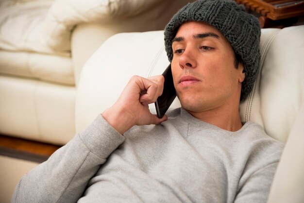 Close-up of young man lying on sofa talking on smartphone