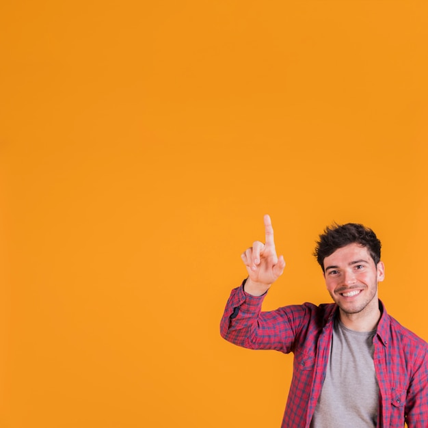 Крупный план молодого человека, указывая пальцем вверх на оранжевом фоне