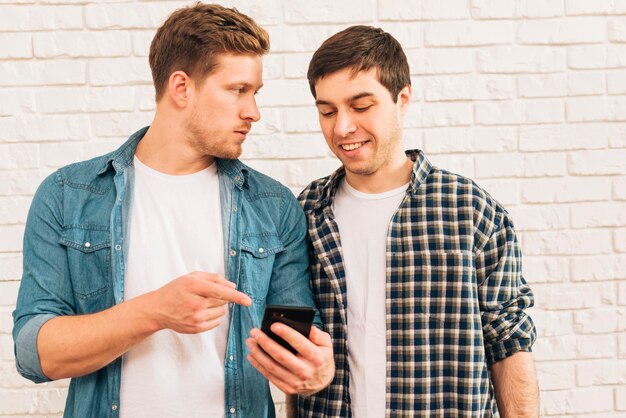 Free photo close-up of a young man showing something on mobile phone to his friend