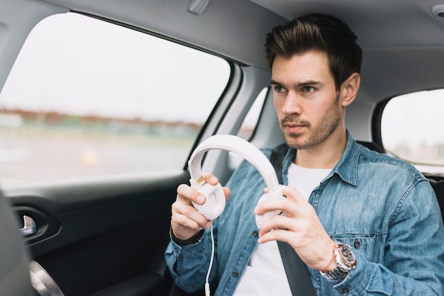 Close-up of a young man travelling in car putting white headphone