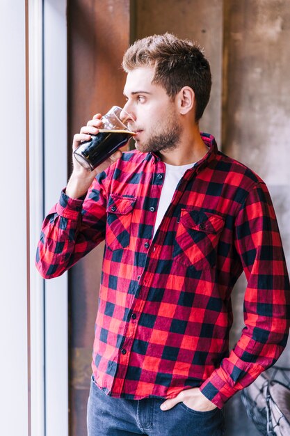 Close-up of a young man with hand in pocket drinking the beer glasses