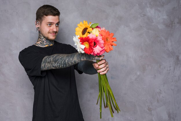 Close-up of young man with tattoo on his body giving beautiful flowers against grey wall