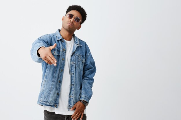 Close up of young men dark-skinned man with afro hairstyle in stylish outfit and sun glasses gesticulating with hands, posing for photo on friend's party.