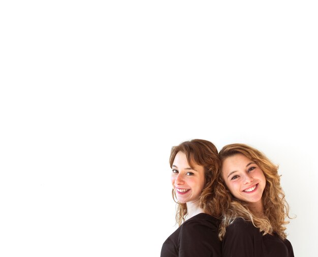 Close-up of young sisters standing back to back standing over white background